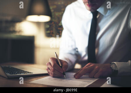 Cropped view of serious businessman signing contract at office, working at night overtime Stock Photo