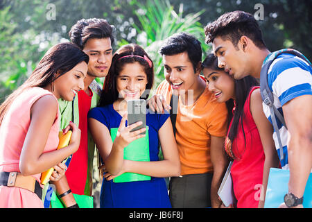 Excited Group Indian Friends Sharing Text Message On Cell Phone In Park Stock Photo
