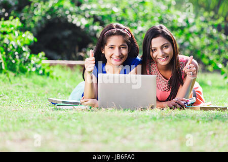 2 Indian College Girls Students Using laptop And Showing Thumbs up Study In Park Stock Photo