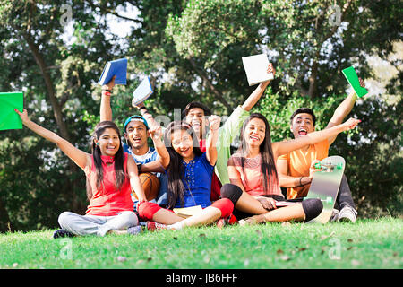 Indian Group College Students Holding Book Cheering Sitting On Grass In Park Stock Photo