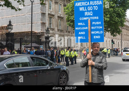 London, UK. 9th June 2017. After election results showed that no party had a majority, protesters came to Westminster to demand that Theresa May resign. She is intending to stay on and try and govern, relying on votes from the DUP party, linked to loyalist paramilitaries. A protester at Downing St holds up a large double-sided placard about the dangers of World War 3 which will kill everyone except 'those GOD want to keep. Credit: ZUMA Press, Inc./Alamy Live News Stock Photo
