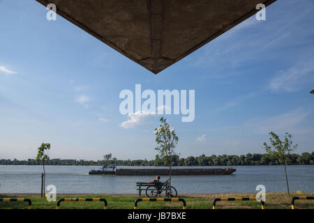 BELGRADE, SERBIA - JUNE 06, 2017: Young man relaxing in front of Danube river, in Belgrade, on Donji Dorcol district, a barge passing by on the water  Stock Photo