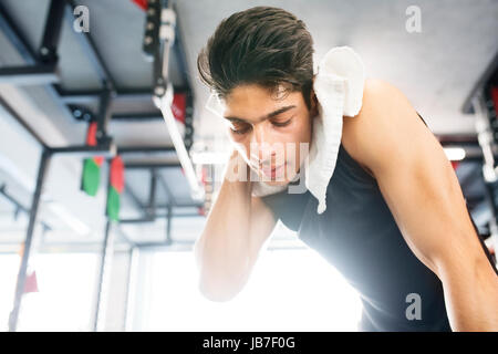 Young fit hispanic man in gym wiping sweat off his face Stock Photo