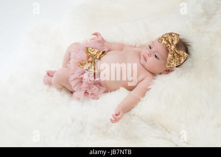 Portrait of a four month old baby girl wearing frilly, pink bloomers and a gold, sequin, bow headband. Shot in the studio on a sheepskin rug. Stock Photo