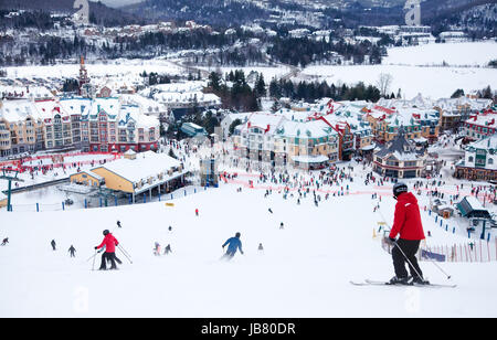 Mont-Tremblant, Canada - February 9, 2014: Skiers and snowboarders are sliding down the main slope at Mont-Tremblant. Mont-Tremblant Ski Resort is acknowledged by most industry experts as being the best ski resort in Eastern North America. Stock Photo