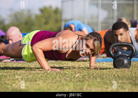 Embarrassed woman doing push-ups with group outdoors Stock Photo