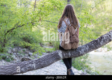 Young girl sitting on a trunk, tree in a forest, in nature Stock Photo