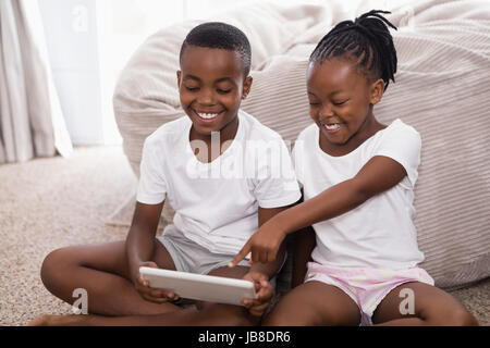 Cheerful siblings using digital tablet while sitting on rug at home Stock Photo