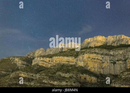 Landscape photo taken at night, during night time with plenty stars in the sky. The cliffs are lit up by the moonlight Stock Photo