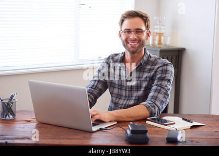 Attractive young, well groomed caucasian male entrepreneur and businessman smiling at the camera with his hands on the keyboard of his laptop computer Stock Photo