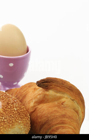 Ausschnitt eines Frühstückstisches mit Brötchen, Croissant und Ei im Eierbecher Stock Photo