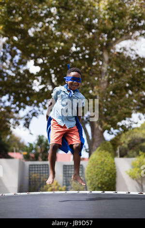 Full length of boy in superhero costume jumping on trampoline Stock Photo