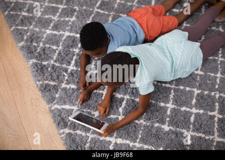 High angle view of siblings using digital tablet while lying on rug at home Stock Photo