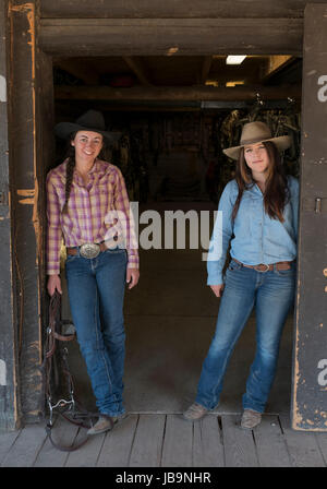 Two young female 'Dude Ranchers' pose for a photograph outside the tack room at the Heart Six Ranch, near Moran junction, Wyoming, USA. Stock Photo
