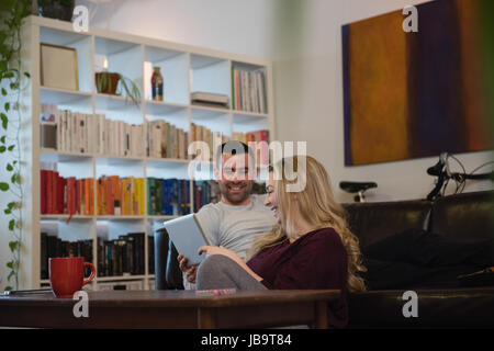 Couple using digital tablet while relaxing on sofa in living room at home Stock Photo