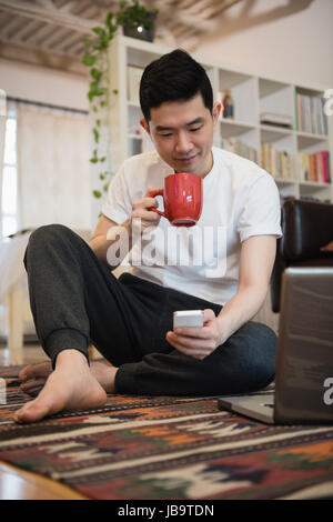 Man using mobile phone while having coffee in living room at home Stock Photo