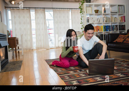 Happy couple using laptop while having coffee in living room at home Stock Photo
