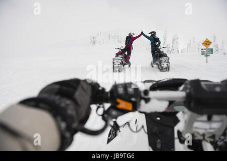 Couple giving high five to each other while riding snowmobile in snowy alps during winter Stock Photo