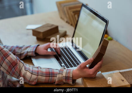 Mid-section of female executive using laptop while holding a wooden slab at desk in office Stock Photo