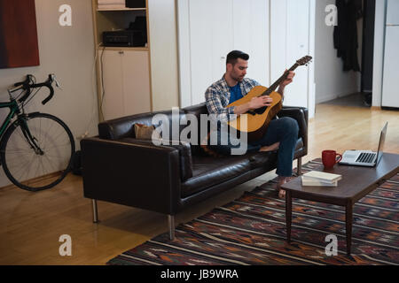 Man playing guitar while relaxing on sofa in living room at home Stock Photo