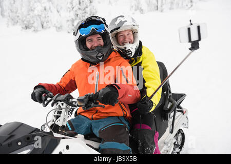 Couple taking selfie on mobile phone while riding snowmobile during winter Stock Photo