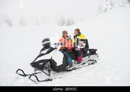 Couple having coffee from thermos while relaxing on snowmobile during winter Stock Photo
