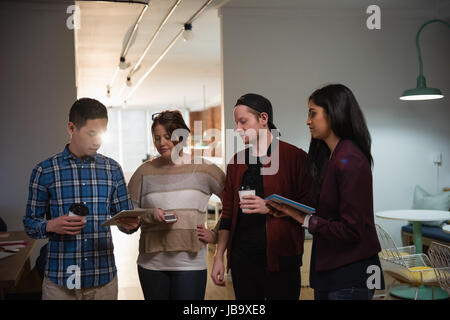 Executives discussing over digital tablet while having coffee in office Stock Photo
