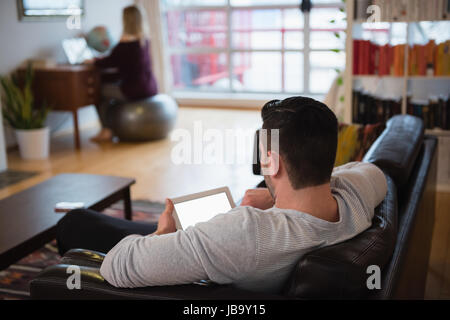 Man using digital tablet while relaxing on sofa in living room at home Stock Photo