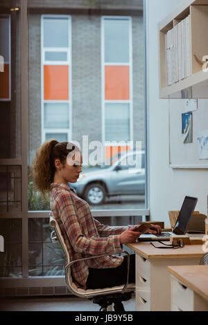 Female executive using laptop while holding a wooden slab in office Stock Photo