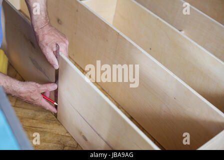 Mature man measuring wooden shelf with ruler while making shelf unit, cropped view of male hands Stock Photo