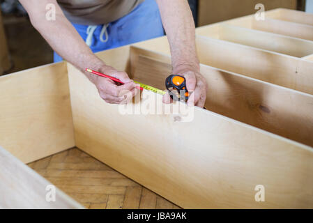 Mature man measuring wooden shelf with reel while making bookcase or shelf unit, cropped view Stock Photo