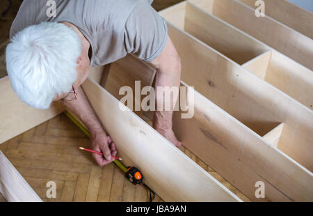 Mature man measuring wooden shelf with reel while making bookcase or shelf unit Stock Photo