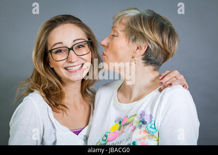 lachende junge enkeltochter mit glücklicher großmutter portrait vor grauem hintergrund