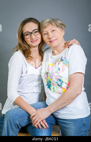 lachende junge enkeltochter mit glücklicher großmutter portrait vor grauem hintergrund