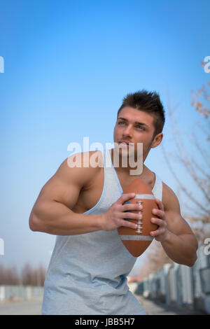 Muscular american football player ready to throw ball in hand. Outdoors shot Stock Photo