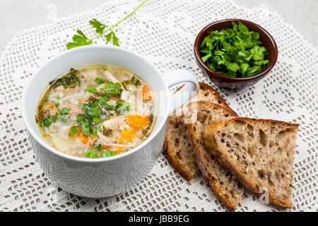 Cup of hot chicken rice soup served with bread and parsley on crochet tablecloth Stock Photo