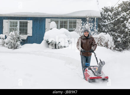 Man using snowblower to clear deep snow on driveway near residential house after heavy snowfall. Stock Photo