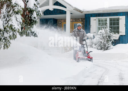 Man using snowblower to clear deep snow on driveway near residential house after heavy snowfall. Stock Photo