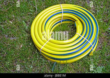 In the garden lies coiled in the form of a round plastic water hose for watering plants in the garden and the vegetable garden. Stock Photo
