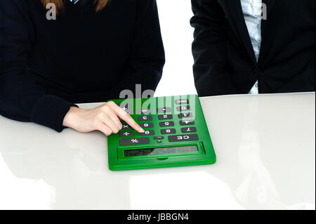 Cropped image of teacher and a student working out on a large green calculator. Stock Photo