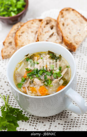 Cup of hot chicken rice soup served with bread and parsley on crochet tablecloth Stock Photo