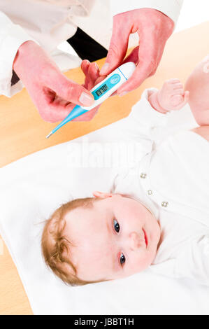 Adult female pediatrician wearing a white coat and a stethoscope and checks with clear in digital thermometer body temperature of the infant, isolated against a white background. Stock Photo