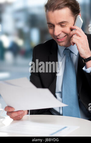 Positive corporate guy communicating on phone with reports in hand Stock Photo