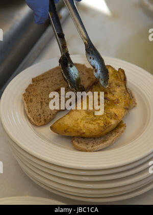 Placing the hot grilled foie gras over bread slices Stock Photo