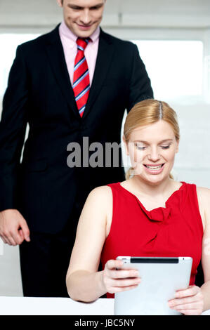Boss operating tablet pc and assistant looking from behind. Office shot Stock Photo