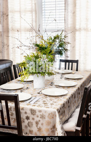 Dining table decorated for Christmas with eight place settings and evergreen centerpiece Stock Photo