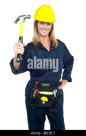 Construction worker in uniform holding up hammer with tool kit around her waist. Stock Photo