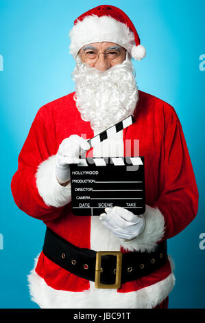 Bespectacled Santa holding a clapperboard. Get ready for next shot. Stock Photo