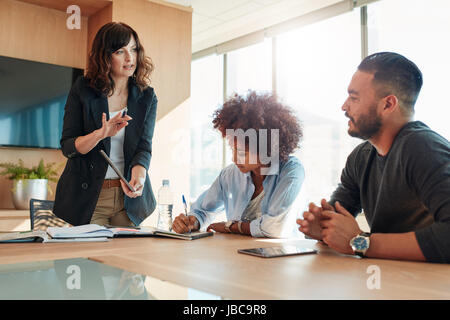 Young businesswoman showing something to her colleagues during a meeting in conference room. Multi ethnic business team discussing project in office. Stock Photo