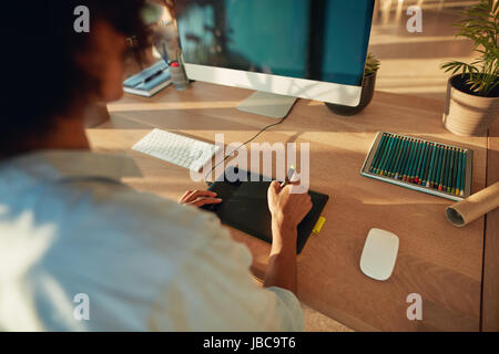 Close up of young female designer using graphics tablet and computer. Woman working at creative workplace. Stock Photo